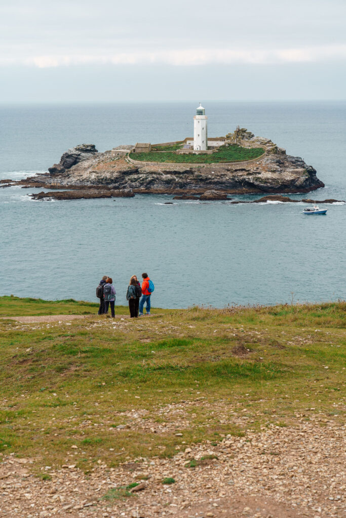 A group of students, hiking along the coast. Godrevy lighthouse is pictured in the background